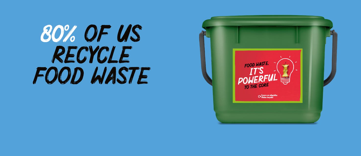 A green food caddy with a red sticker on a blue background with the words "80% of us recycle food waste"
