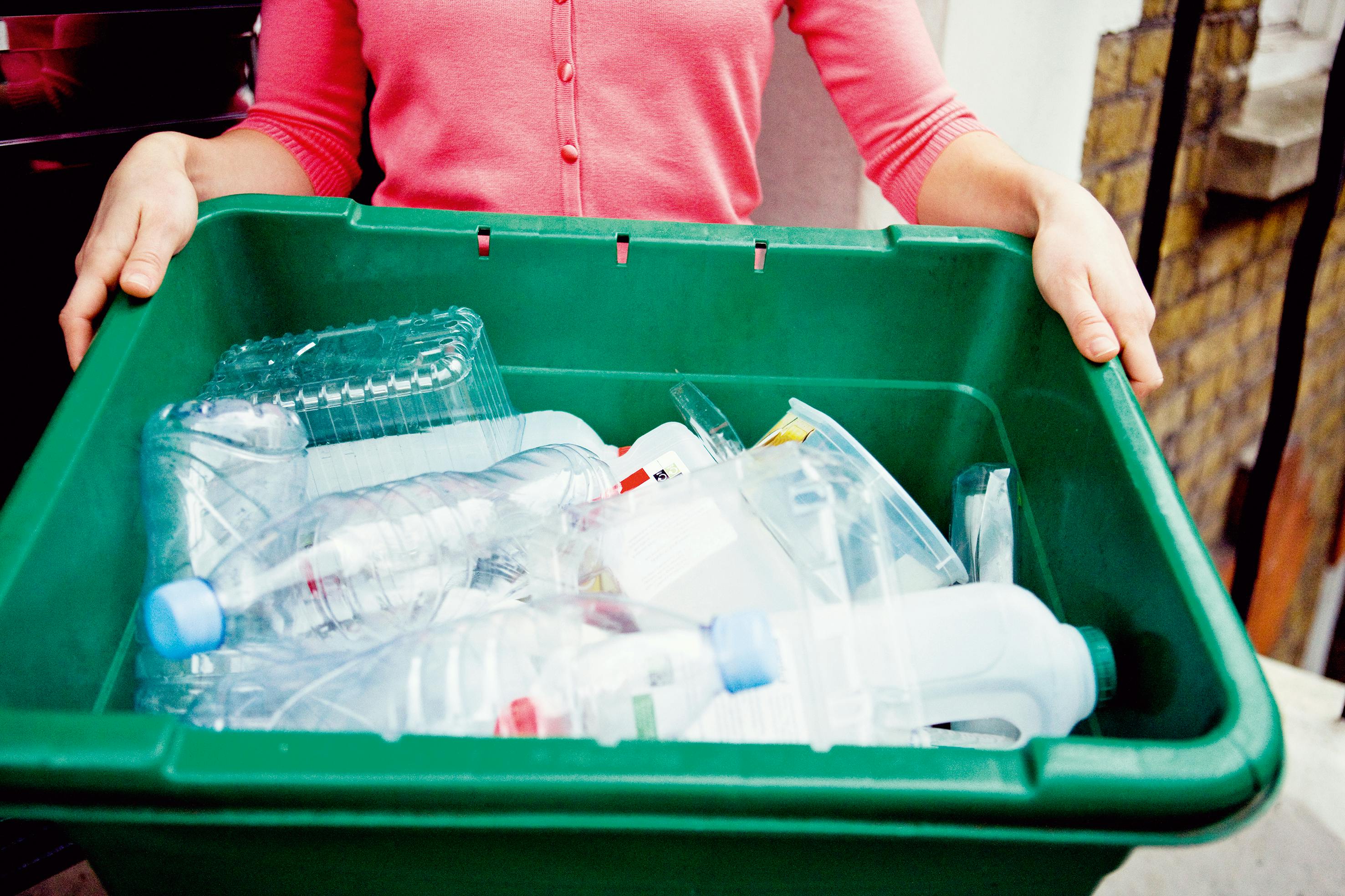 A person holding a green recycling box containing plastic bottles