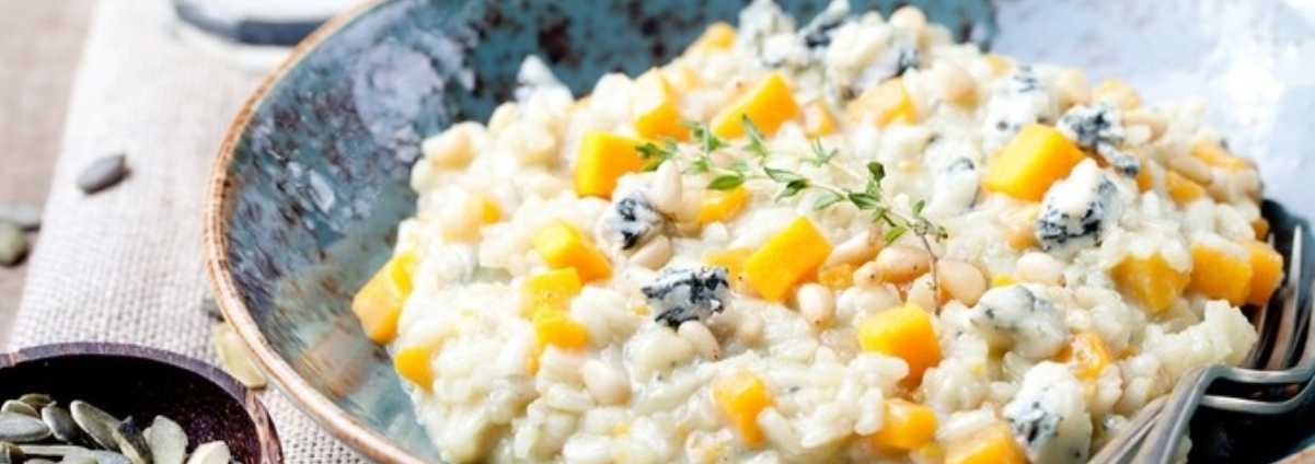 A bowl of risotto with vibrant orange pumpkin pieces scattered in.